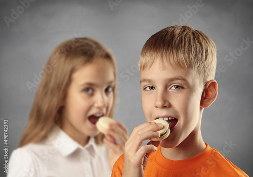 Boy and girl eatind cakes on grey background.