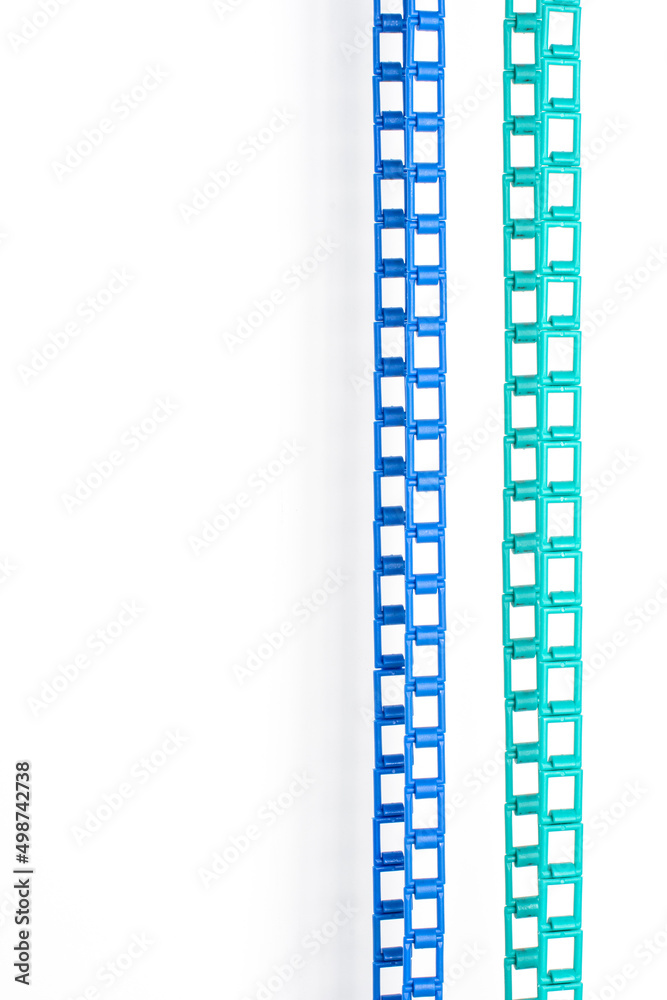 Blue and green plastic chains are hanging on a white wall. Vertical picture.