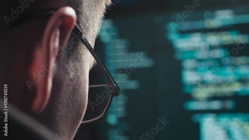 The face of a male computer scientist close-up. The programmer types the code for the program. Symbols appear quickly on the monitor screen. Guy with glasses