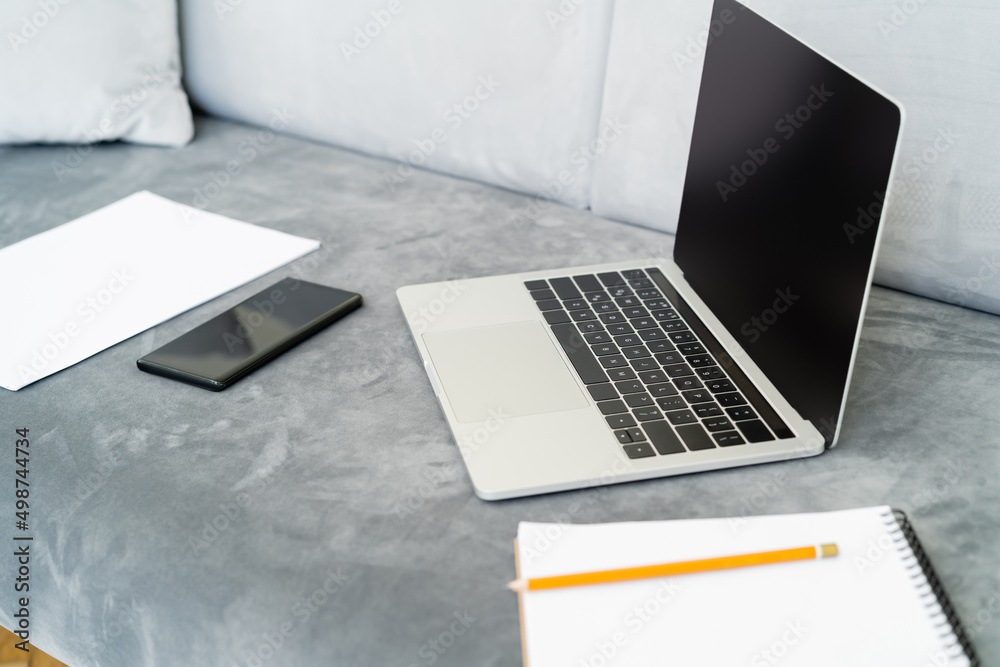 mobile phone and laptop with blank screen near blurred notebook on grey sofa. mobile phone and laptop with blank screen near blurred notebook on grey sofa.