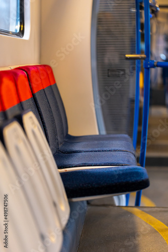 Empty interior of a commuter train during a pandemic. A view of a series of chairs along the windows. Interior lighting is on.