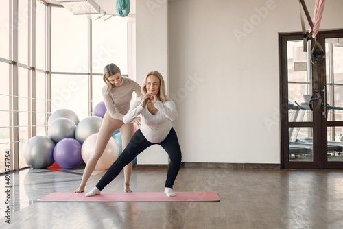 Trainer helping pregnant woman to do yoga asana