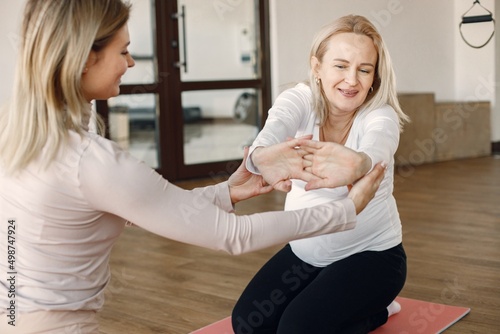 Trainer helping pregnant woman to do yoga asana