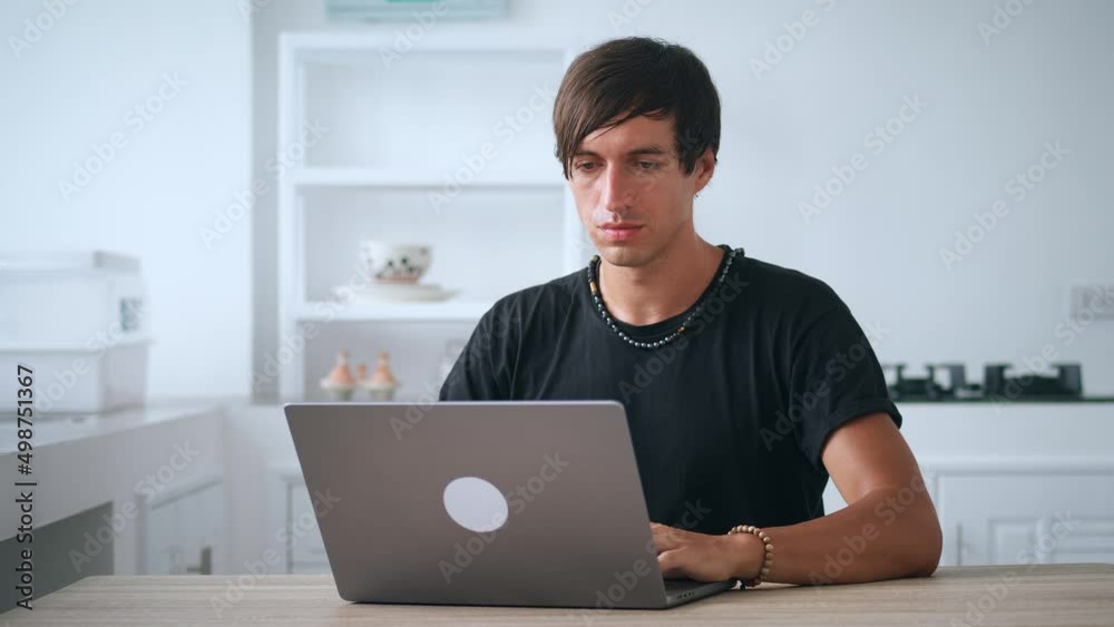 Young business male freelancer working at laptop while sitting at kitchen table at home. Home workplace. Home office. Young business male freelancer working at laptop while sitting at kitchen table at home. Home workplace. Home office.