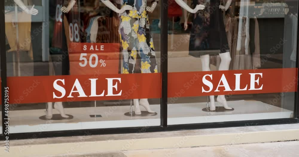 Glass of shop window showcase with discount sticker on the city street. Boutique with clothes on big sale. Offline shopping, store mannequins with red price tags