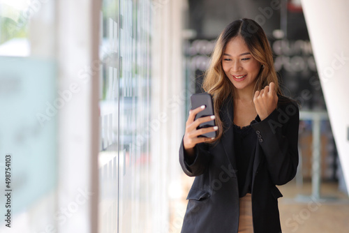 Asian female employees express the excitement of success and bonuses. Asian businesswoman in formal suit in office happy and cheerful during using smartphone and working.
