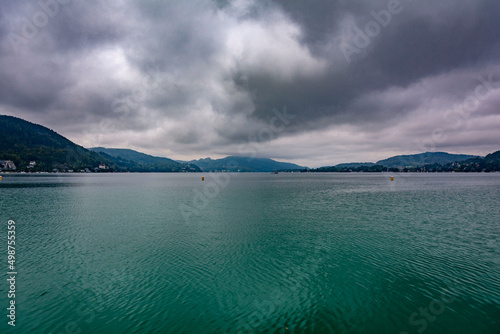Mirrored calm lake water, mountains in the background, cloudy dark sky in an autumn morning