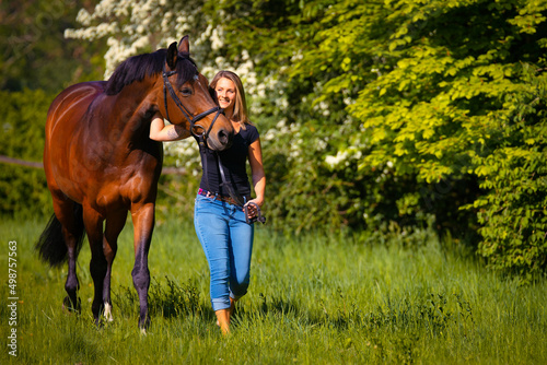 A horse and a young woman walk across a green meadow, the horse snuggles up to its owner.. © RD-Fotografie