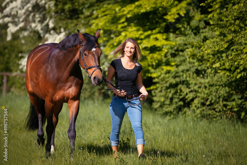 A horse and a young woman are walking across a green meadow, the girl is smiling at her horse.. © RD-Fotografie
