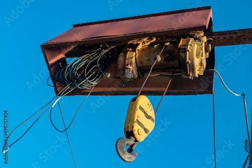 Electric cable hoist with black hook in yellow casing.