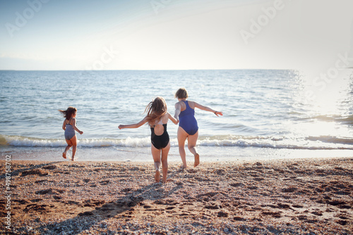 Three children of girls in swimsuits run on the sand and play on the beach. Summer holidays and adventures of siblings. Active games on the sea coast. overweight child