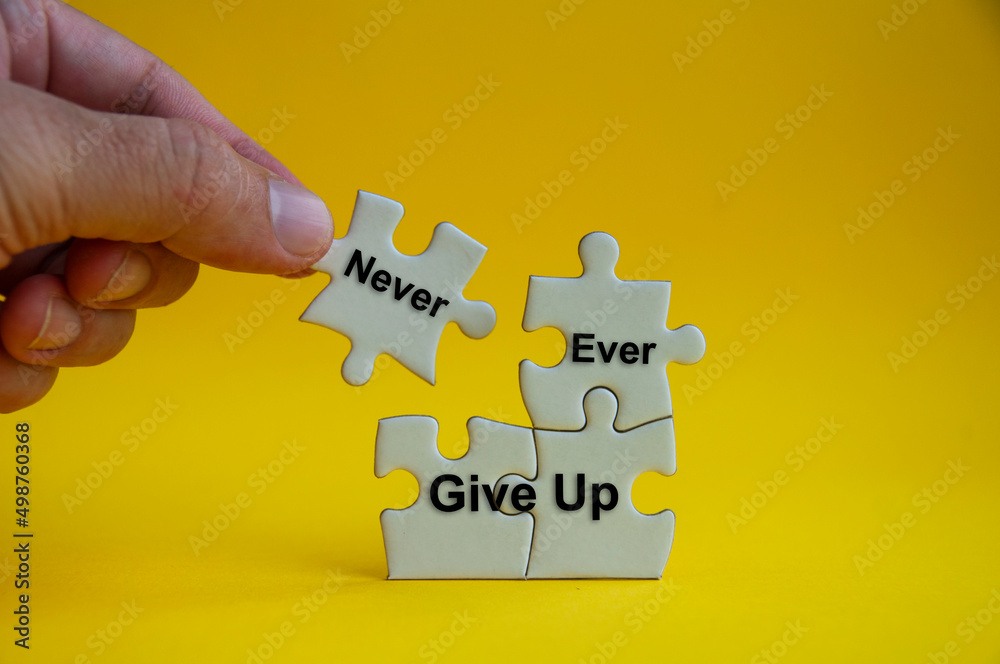 Motivational text on jigsaw puzzle with hand holding a missing jigsaw - Never ever give up. - obrazy, fototapety, plakaty 