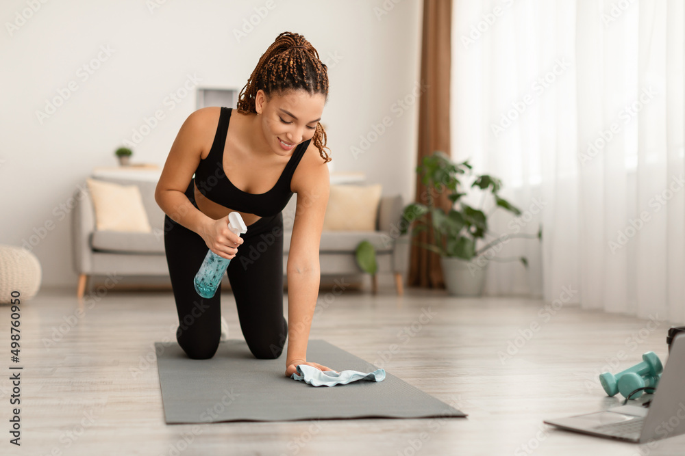 Fototapeta premium Black Fitness Woman Cleaning Gymnastics Mat Before Workout At Home