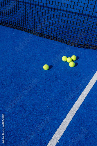 several paddle tennis balls by the net on a blue paddle tennis court © Vic