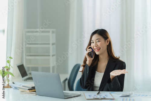 Asian business woman using smart phone and laptop in office.