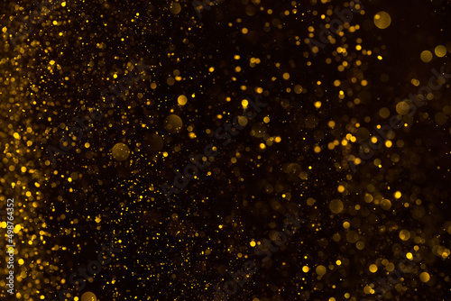 Abstract golden glitter shiny particles lights dark bokeh pattern background