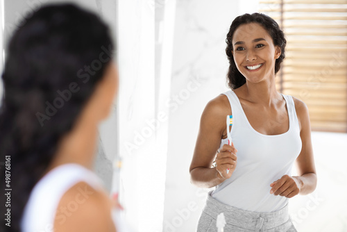 Attractive Millennial Woman With Toothbrush In Hand Posing Near Mirror In Bathroom © Prostock-studio