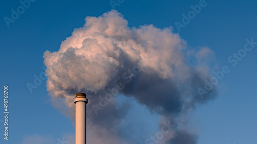 the smog above an industrial chimney on a clear blue sky background. 