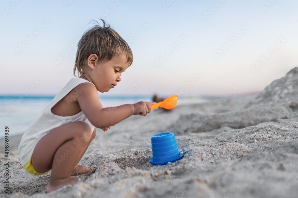 Boy playing with toys on the beach building beads and turrets smiling at someone behind the scenes on summer vacation Boy playing with toys on the beach building beads and turrets smiling at someone behind the scenes on summer vacation