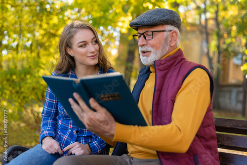 Fotografija Grandfather and granddaughter looking at photo album in park