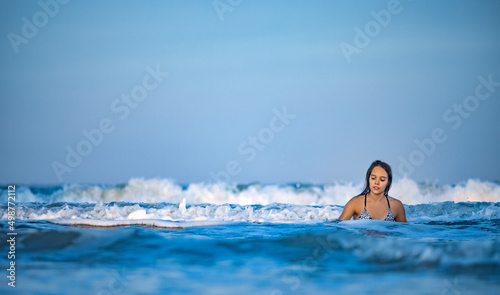 Girl with wet hair in a leopard swimsuit splashes water while sitting in the sea
