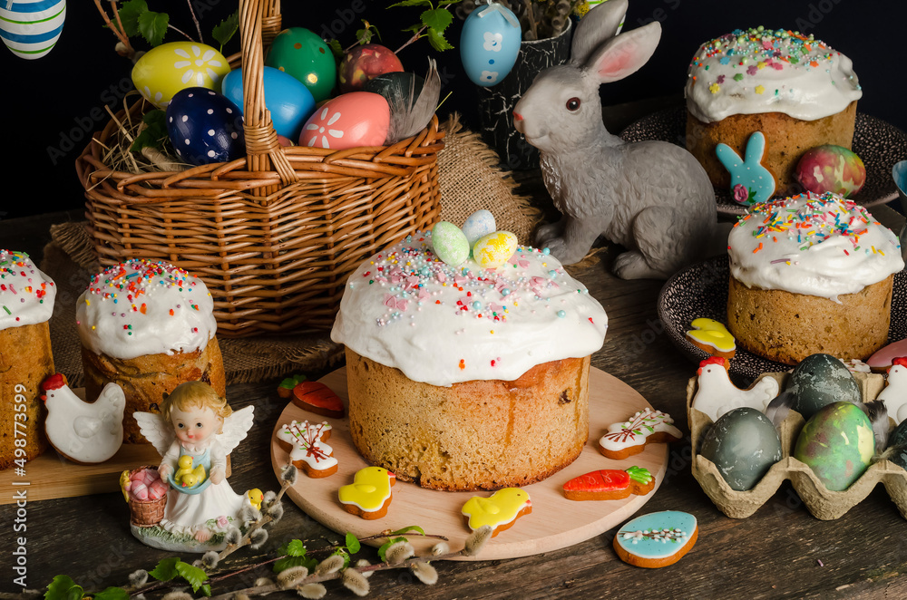 Easter cakes and eggs on a festive Easter table with willow and a figurine of a rabbit on a dark background