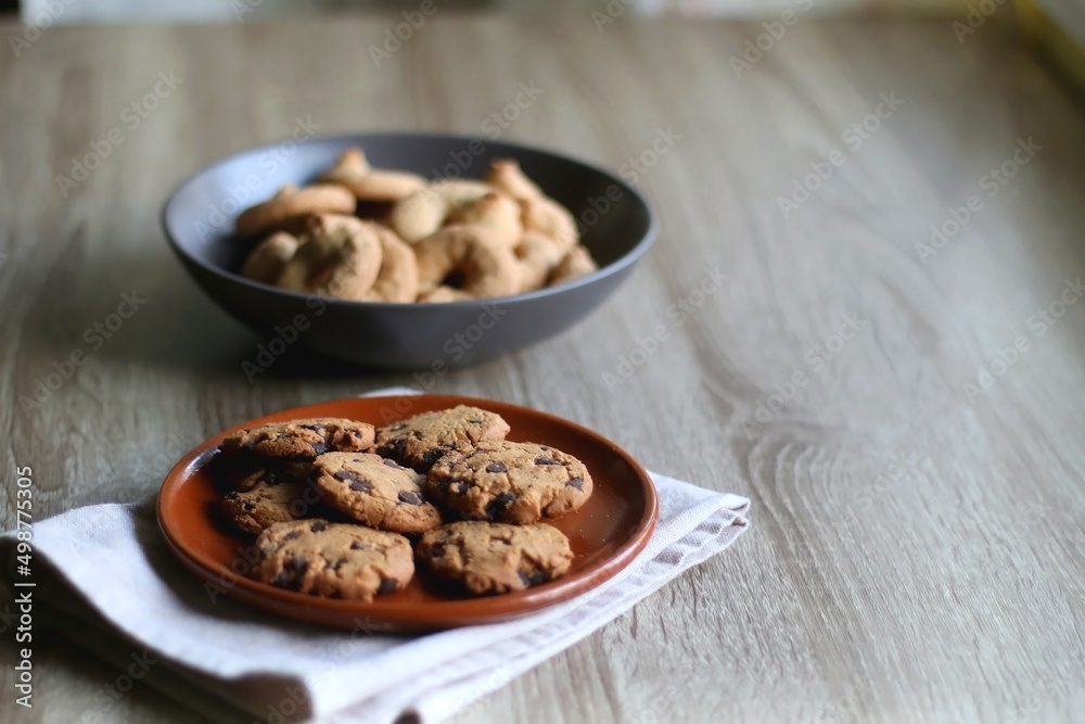 Plate of chocolate chip cookies and bowl of sugar cookies on wooden table. Selective focus. Plate of chocolate chip cookies and bowl of sugar cookies on wooden table. Selective focus.