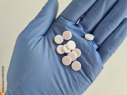 Hand in glove and white medical pills closeup photo