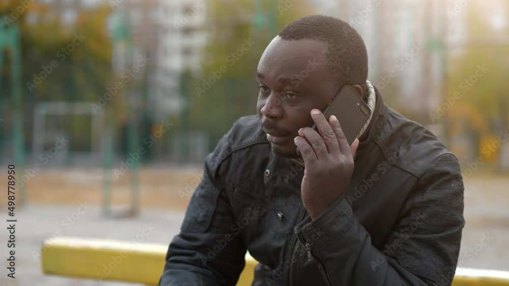 Slow Motion African american man sits at sport ground and speaks on smartphone Slow Motion African american man sits at sport ground and speaks on smartphone