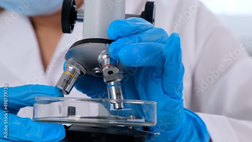 Hands of a researcher laboratory assistant in protective gloves holding a microscope in the laboratory, close up.