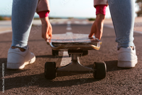 Woman holding her longboard with both hands on the promenade ready to start the march. Young girl placing her skate in the right lane of a beach asphalt and the air ahead.