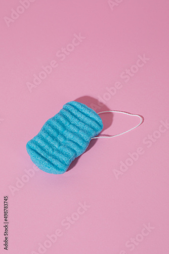 Blue washcloth on a pink background. Cosmetic item for skin cleansing. Porous washcloth for cleansing the skin. Skin care. Conceptual picture. Close-up. Abstraction photo