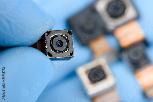 Smartphone camera module in researcher hand, with other cell phone camera sensor on background.