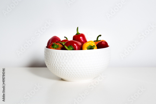 Fototapeta Naklejka Na Ścianę i Meble -  Selective focus horizontal shot of red, orange and yellow mini bell peppers in white bowl set on white background