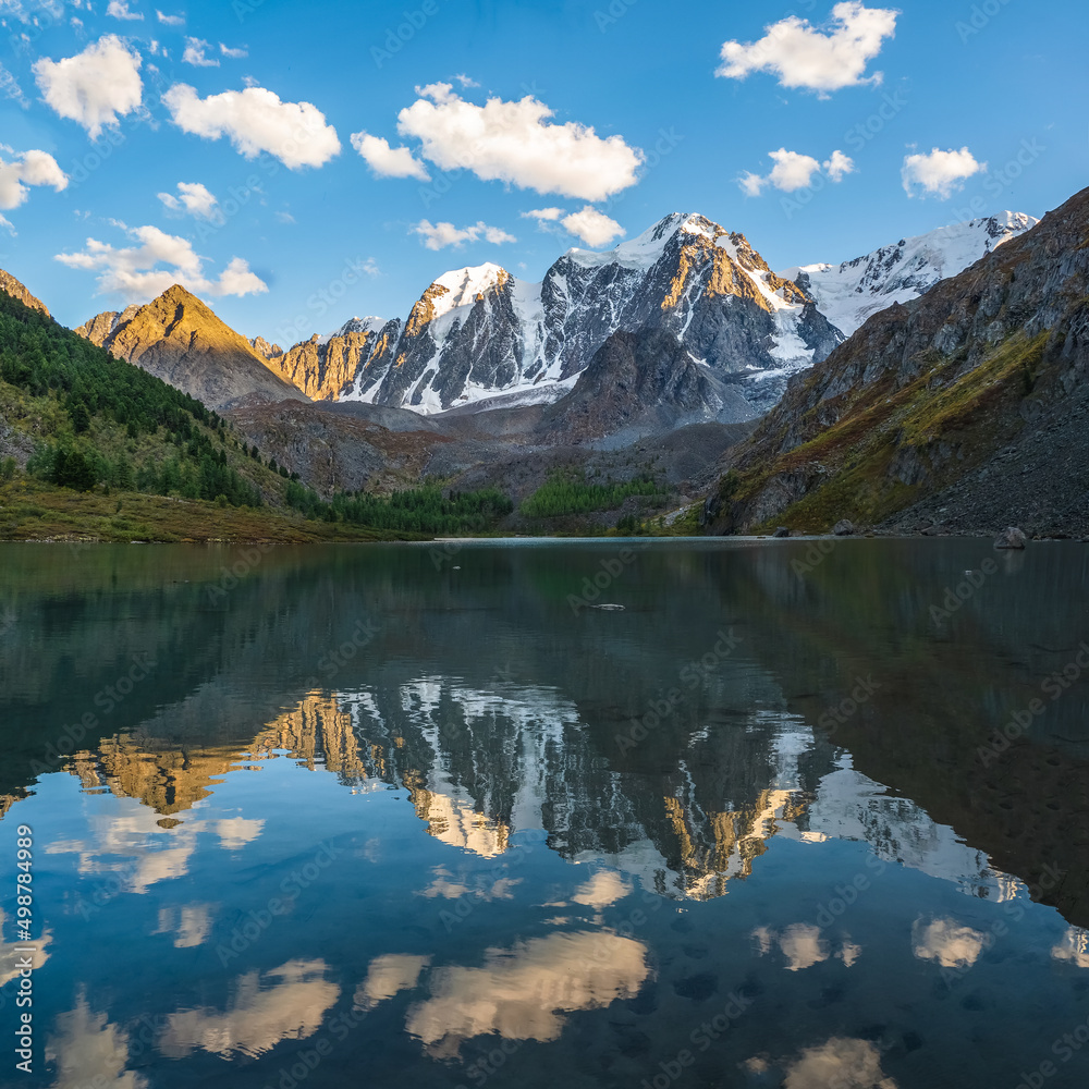 Beautiful evening landscape with glacier reflection in water surface of mountain lake. Snowy mountain reflected in clear water of glacial lake. Snow on rock reflected in mountain lake.