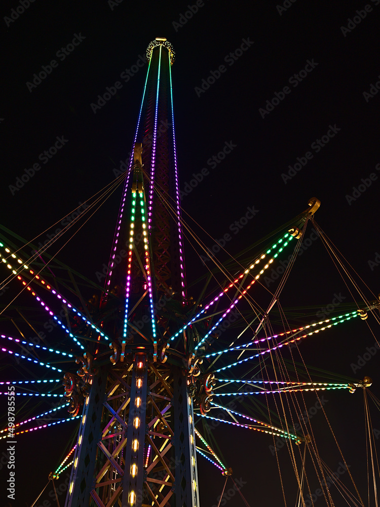 Low angle view of drop tower with colorful, illuminated structure at night in amusement park Wurstelprater near Wiener Prater in city Vienna, Austria.