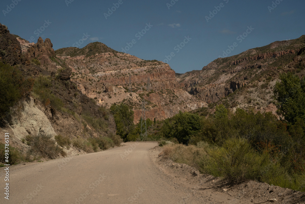 Travel. View of the dirt road across the arid desert and colorful rock formations.	
