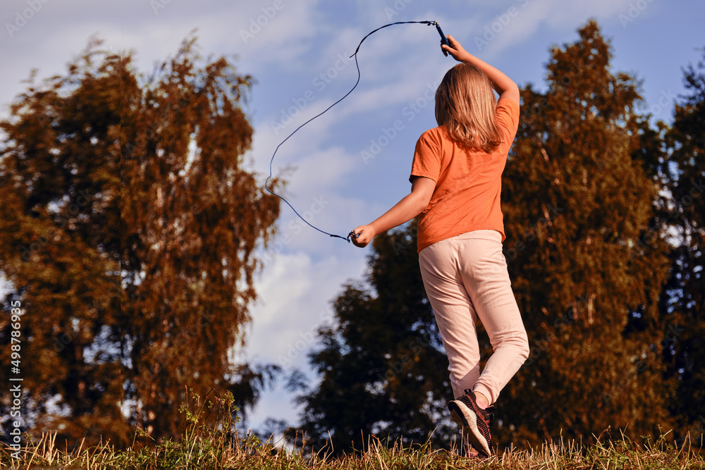Child jumping rope in the park on a sunny day. A ten-year-old girl goes ...