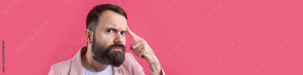 Obraz premium Handsome man with a beard in a pink jacket is thinking over an isolated red background.