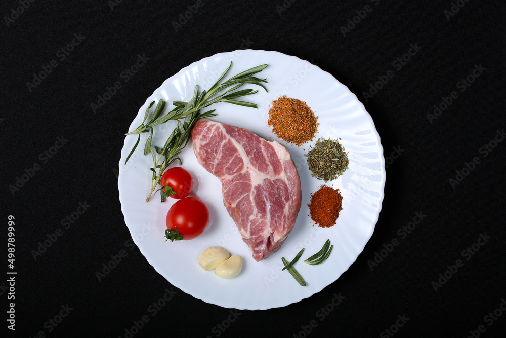 Fresh steak with spices and vegetables on a white plate and black background