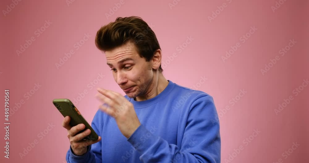 Young man having fun while using mobile phone over pink background Young man having fun while using mobile phone over pink background