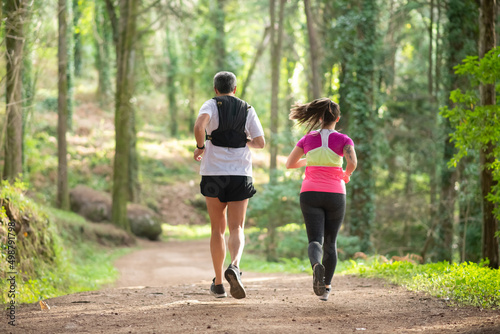 Back view of energetic man and woman jogging in forest. Two sporty people in sportive clothes exercising outdoors. Sport, hobby concept