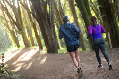 Fototapeta Naklejka Na Ścianę i Meble -  Back view of enthusiastic man and woman jogging in forest. Two sporty people in sportive clothes exercising outdoors. Sport, hobby concept