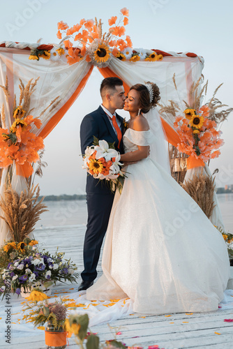 Loving couple at an international wedding at sunset. Beautiful sophisticated bride of Asian appearance. Strong manly groom of Caucasian appearance. Mixed marriages. Warm embrace.
