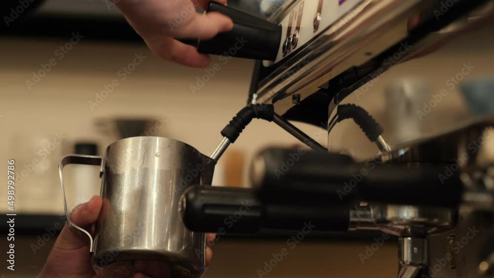 Barista male hands holding stainless steal jug. Steam wand of coffee machine and release foggy hot steam to reheat or warm milk for latte coffee cup, closeup Barista male hands holding stainless steal jug. Steam wand of coffee machine and release foggy hot steam to reheat or warm milk for latte coffee cup, closeup