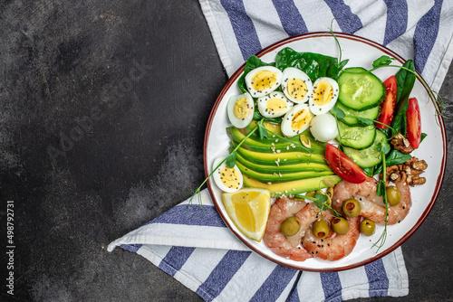 Ketogenic breakfast. Keto low carb shrimps, prawns, quail eggs, fresh salad, tomatoes, cucumbers and avocado on a dark background. keto diet. Top view
