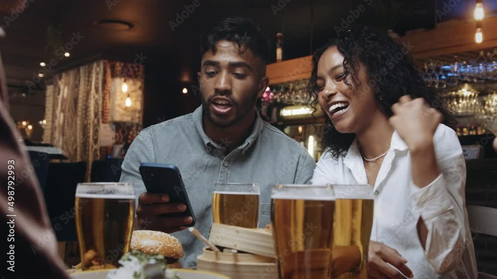 Two multiracial friends at a restaurant looking at the selfies they took on one of their mobile phones. Two multiracial friends at a restaurant looking at the selfies they took on one of their mobile phones.