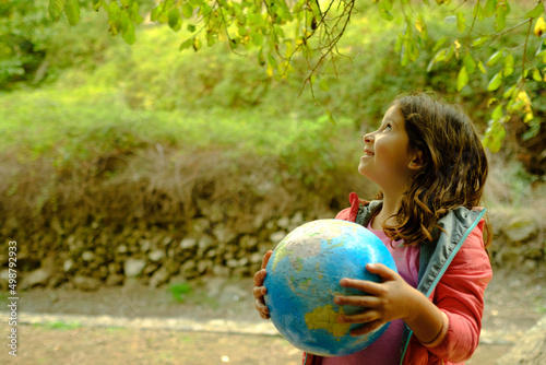 a girl holds a globe with both hands while looking up in the middle of nature.