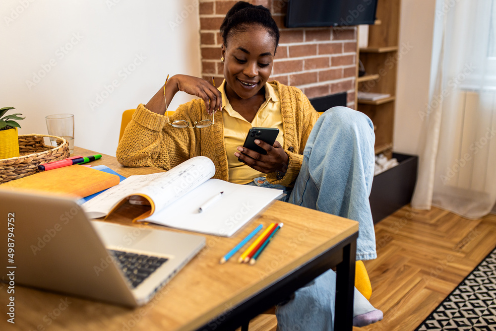 Young African American woman working from her living room using smartphone. Young African American woman working from her living room using smartphone.