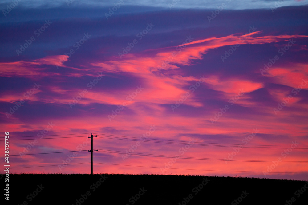 Colorful sky at sunrise with silhouetted power line and pole